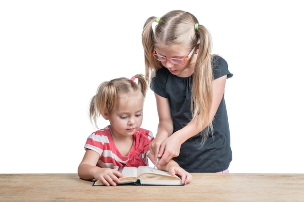 Sœur aînée apprend au plus jeune à lire un livre posé sur une table en bois isolée sur fond blanc