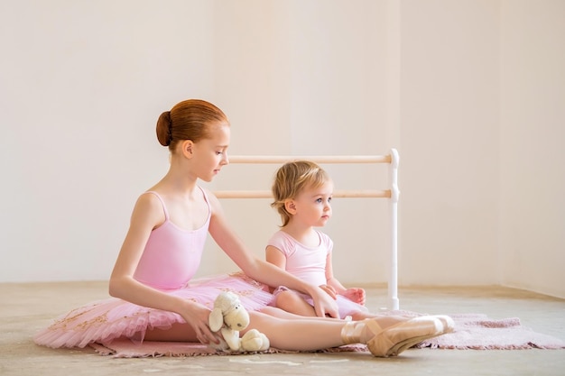 La sœur aînée une ballerine en tutu rose et chaussons de pointe montre au bébé comment pratiquer à la barre