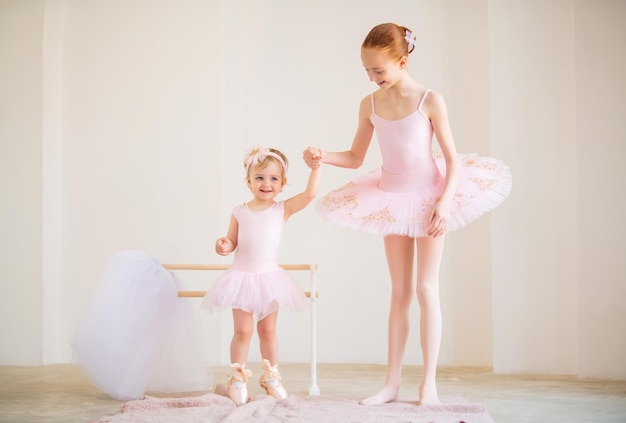La sœur aînée une ballerine en tutu rose et chaussons de pointe montre au bébé comment pratiquer à la barre