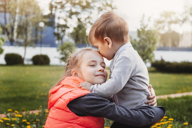 La sœur aînée embrasse son petit frère en été dans le parc