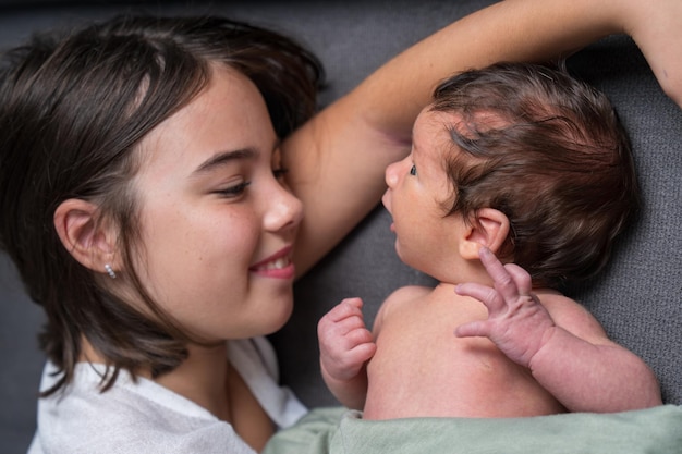 Une sœur aînée et un frère nouveau-né sont allongés sur le canapé. La fille regarde le bébé avec amour