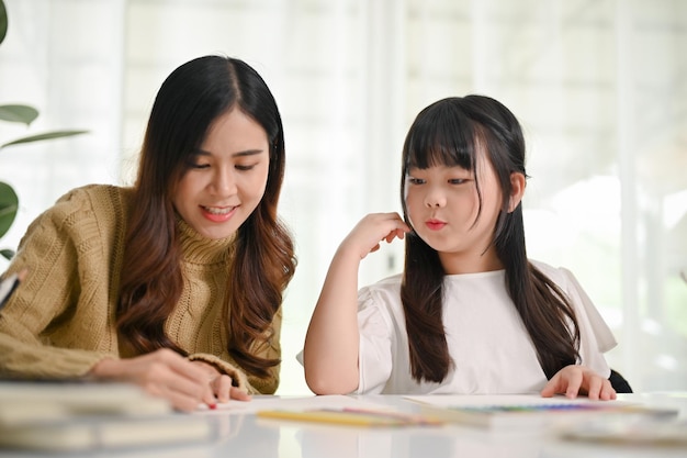 Sœur asiatique attentionnée aidant sa petite sœur à peindre avec des pastels à l'huile à la maison