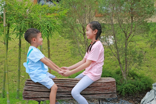 Soeur asiatique contact avec les yeux frère et main dans la main tout en étant assis sur un banc en bois dans le jardin