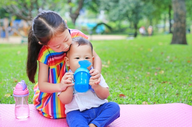 Photo soeur asiatique prend soin de son petit frère à l'eau potable de bébé tasse à bébé avec de la paille