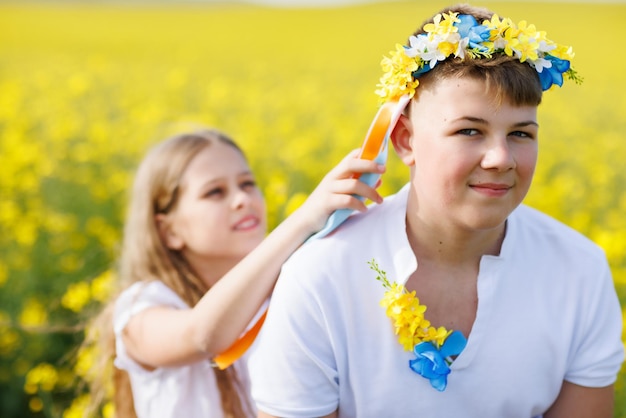Sœur tresse des rubans dans une couronne ukrainienne sur la tête de son frère adolescent sur fond de champs et de ciel