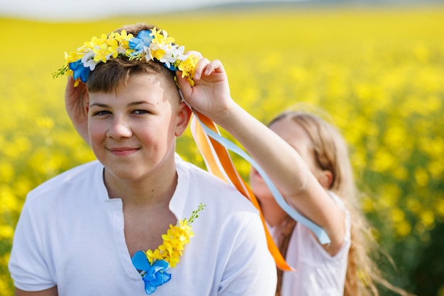 Sœur tresse des rubans dans une couronne ukrainienne sur la tête de son frère adolescent sur fond de champs et de ciel