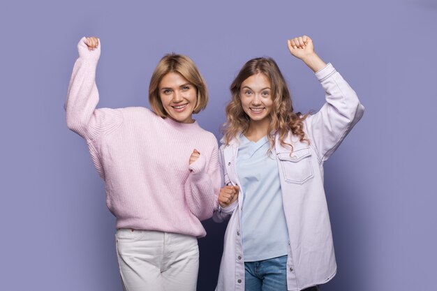 Les sœurs dansantes encouragent un mur violet souriant à la caméra en levant les mains