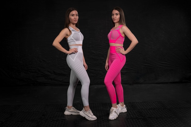 Sœurs jumelles en vêtements de fitness posant sur un fond sombre