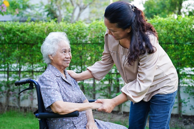 Le soignant aide une femme âgée asiatique handicapée patiente assise sur un fauteuil roulant dans le concept médical du parc