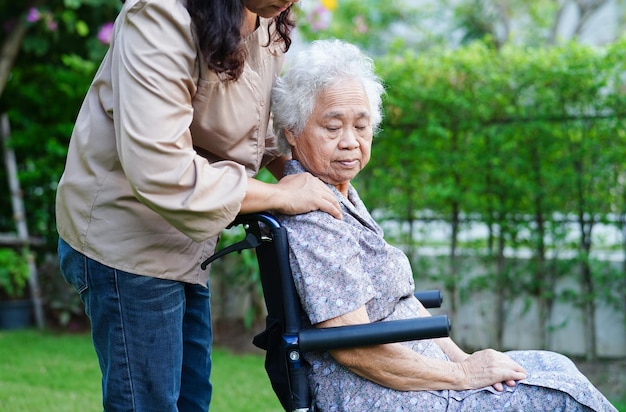 Le soignant aide une femme âgée asiatique handicapée patiente assise sur un fauteuil roulant dans le concept médical du parc
