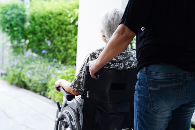 Un soignant aide une femme âgée asiatique handicapée patiente assise sur un fauteuil roulant à l'hôpital médical