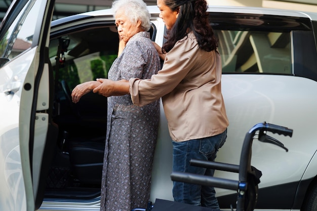 Un soignant aide une patiente asiatique âgée handicapée à entrer dans son concept médical de voiture