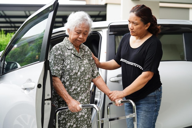 Photo un soignant aide une patiente asiatique âgée handicapée à entrer dans son concept médical de voiture