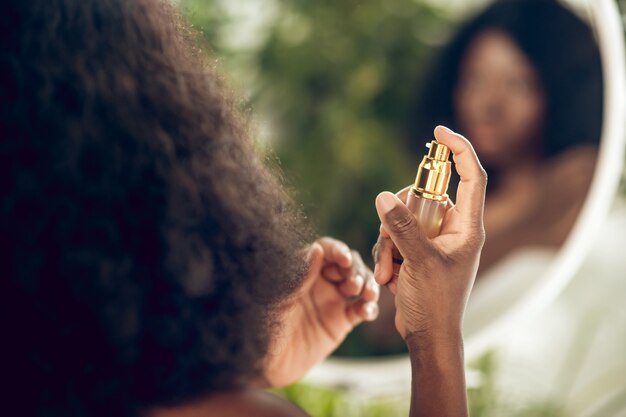 Soin des cheveux. Attrayant femme afro-américaine de pulvérisation de sérum sur ses cheveux