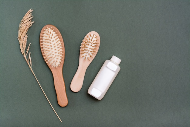 Soin des cheveux. Deux peignes en bois, une bouteille de shampoing et des épis d'herbes sur fond vert.