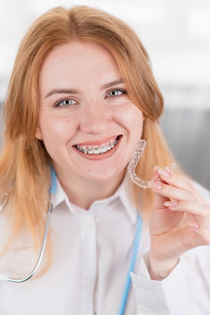 Soin dentaireUne fille souriante avec des accolades sur ses dents tient des gouttières dans ses mains et montre la différence entre elles