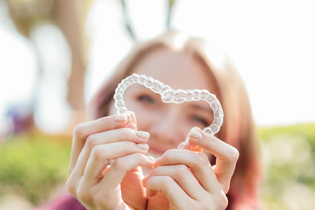 Soin dentaireUne fille souriante avec des accolades sur ses dents tient des gouttières dans ses mains et montre la différence entre elles