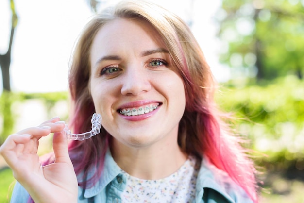 Soin dentaireUne fille souriante avec des accolades sur ses dents tient des gouttières dans ses mains et montre la différence entre elles