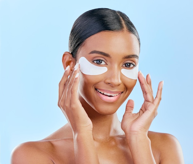 Soin de la peau heureux et portrait de femme avec des patchs pour les yeux cernes et traitement Visage souriant et fille indienne ou modèle avec un collagène facial pour une lueur isolée sur fond bleu en studio