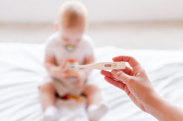 Soins bébé. Main tenant un thermomètre pendant que bébé est assis sur le lit