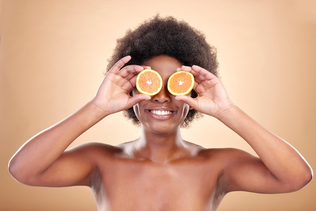 Soins de la peau aux fruits orange et femme sur fond de studio pour les cosmétiques naturels, les bienfaits sains et la nutrition Un modèle de beauté africain heureux couvre les yeux avec des agrumes pour la détox à la vitamine C ou la dermatologie écologique