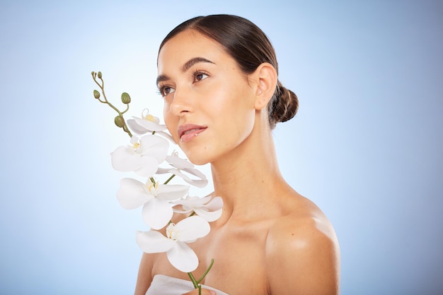 Soins de la peau de beauté et femme avec une orchidée dans un studio pour une routine de bien-être et de visage naturel Soins cosmétiques et modèle de fille à la peau claire du soin du visage au spa sur fond bleu