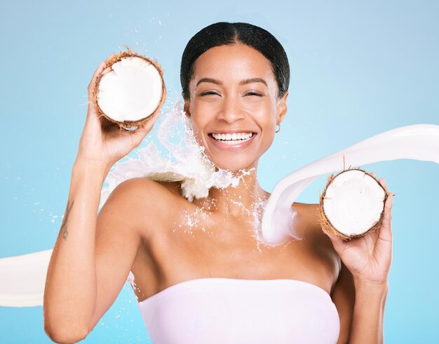 Soins de la peau beauté et portrait de femme avec noix de coco pour une peau et une alimentation saines sur fond bleu Visage d'une personne modèle esthétique avec des éclaboussures de lait et des fruits pour une santé et un bien-être faciaux durables