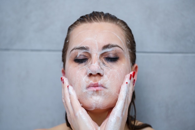 Soins de la peau du visage. Femme appliquant un nettoyant pour le visage sur le visage agrandi. Fille utilisant un produit cosmétique nettoyant sur la peau, se lavant le visage sur fond clair