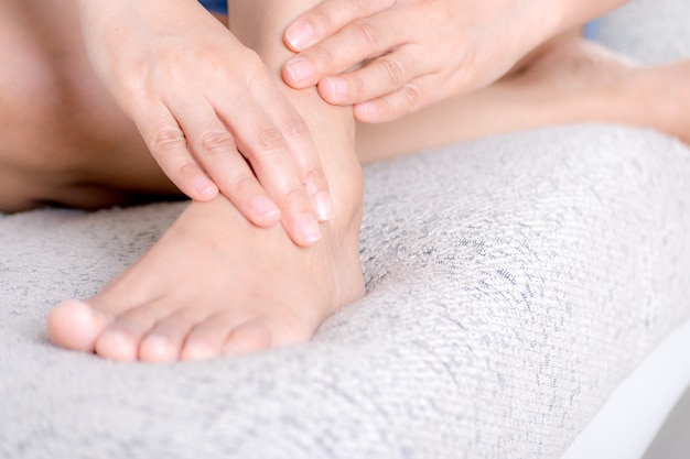 Soins de santé et concept médical. Closeup jeune femme assise sur un canapé et se sentant la douleur à la cheville et elle se masser la cheville à la maison.