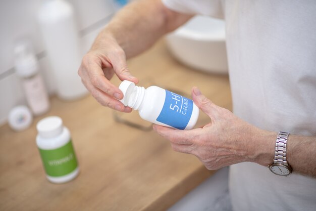 Soins de santé. Homme aux cheveux gris en tshirt blanc avec des bouteilles de vitamines dans ses mains