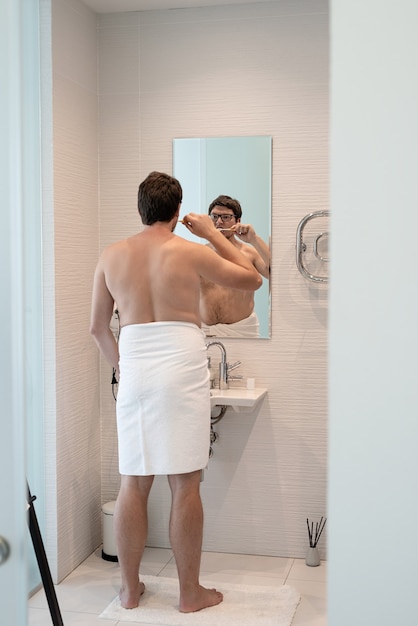 Soins de santé, hygiène dentaire. Jeune homme adulte se brosser les dents dans la salle de bain, regardant le miroir