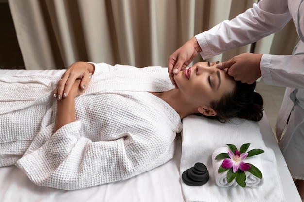 soins spa une jeune femme reçoit un massage du visage en position allongée sur un canapé dans un salon d'élite.