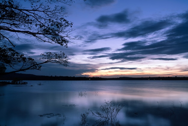 Soir ciel nuages au coucher du soleil sur le lac derrière la silhouette de branche d&#39;arbre.