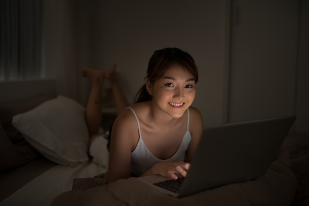 Soirée chambre à coucher - femme avec ordinateur portable couchée dans son lit