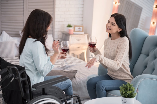 Soirée girly. Heureuse femme handicapée et ami buvant du vin et bavardant