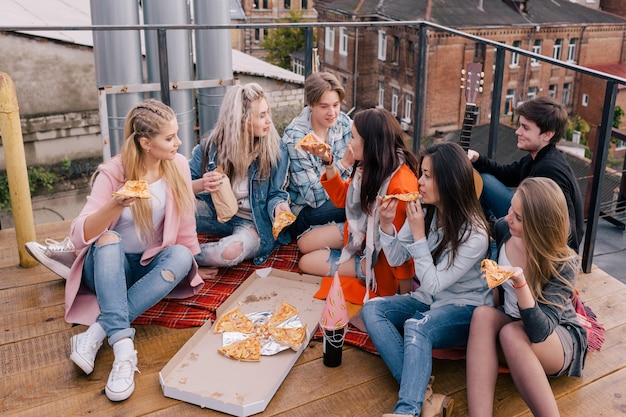 Soirée pizza entre amis sur le toit. Communication ensemble à l'extérieur, nourriture malsaine, jeunes en fête