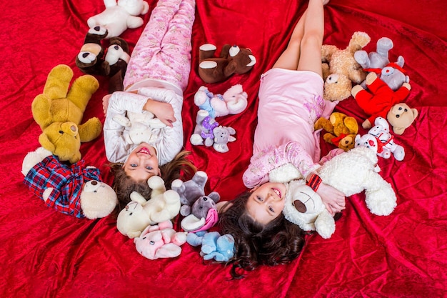 Soirée pyjama Vêtements d'intérieur pour enfants Enfants en pyjama doux et chaud jouant à la maison Les filles en pyjama coloré tiennent des animaux en peluche drôles le bonheur de l'enfance Les sœurs filles en pyjama se trouvent dans le lit vue de dessus