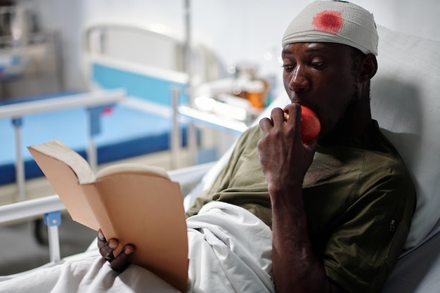 Soldat afro-américain mangeant des fruits et lisant un livre en position couchée dans un hôpital militaire après une blessure