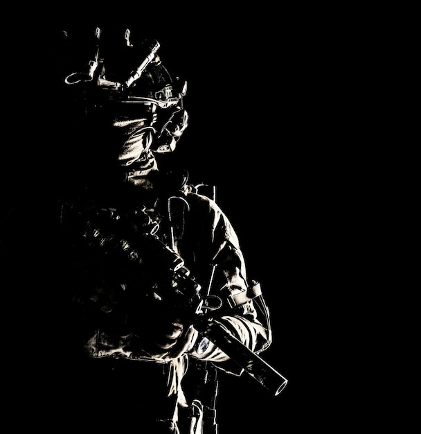 Photo soldat des forces d'opérations spéciales de l'armée en masque et uniforme de combat casque équipé d'un dispositif de vision nocturne mitraillette armée avec silencieux regardant de côté portrait de studio discret sur fond noir