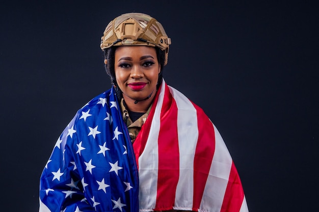 Soldat latin de l'armée afro-américaine en vêtements de camouflage cheveux dreadlocks maquillage de soirée et grandes lèvres sur fond noir dans le studio avec drapeau américain jour de l'indépendance usa 4 juillet
