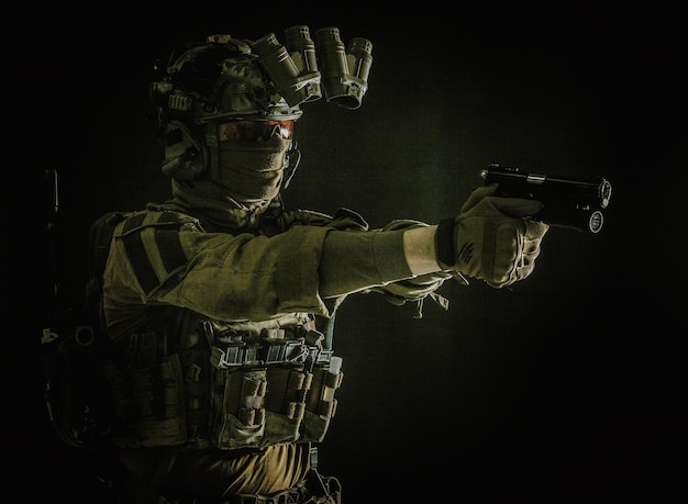 Soldat moderne combattant de l'escouade anti-terroriste dans un casque uniforme de combat et un casque radio tactique visant un pistolet de service dans l'obscurité tirant avec un portrait de studio d'arme de poing sur fond sombre
