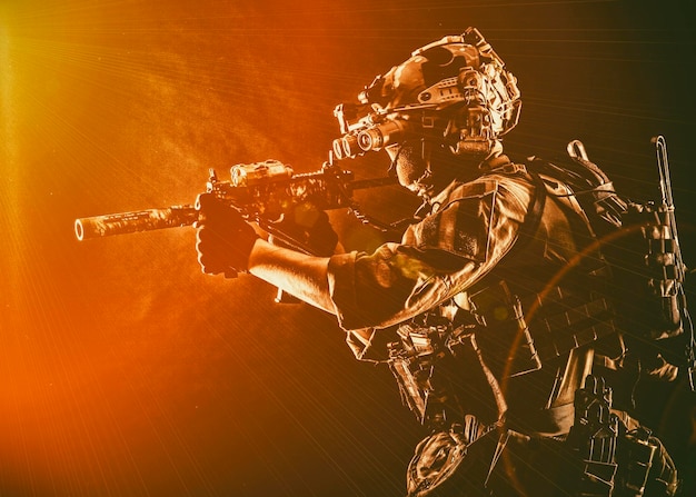 Photo soldat d'opérations spéciales de l'armée combattant commando dans un casque de munitions tactique complet avec casque radio et dispositif de vision nocturne visant un fusil d'assaut à canon court dans l'obscurité tournage en studio discret