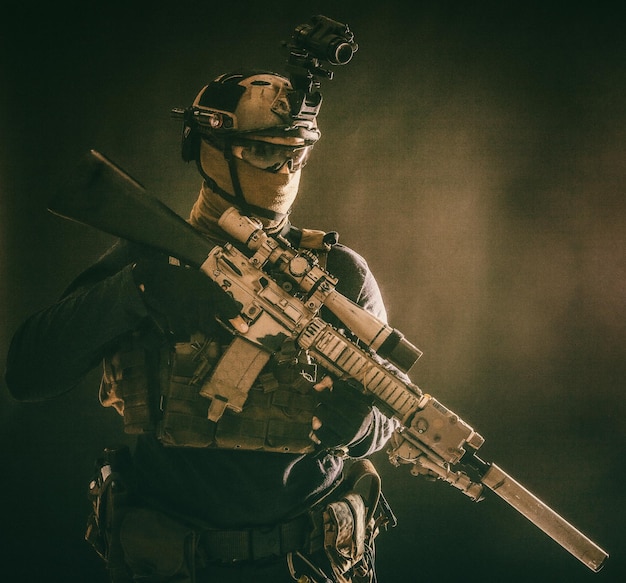 Photo soldat d'opérations spéciales de l'armée contre-terroriste équipage tireur d'élite tireur d'élite dans un casque de combat se cachant le visage derrière un masque fusil de service blindé avec vue optique tournage en studio discret sur fond bleu