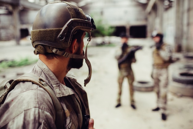Un soldat qui porte l'uniforme regarde ses amis. Ils se tiennent assez loin de lui. Les gars se reposent.