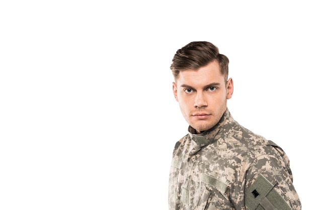 Soldat sérieux et beau en uniforme regardant la caméra isolée sur blanc