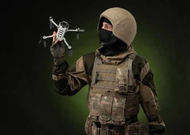 Un soldat en tenue militaire avec une arme lance un petit quadricoptère sans pilote pour la reconnaissance sur fond sombre