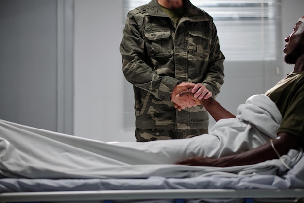 Soldat en uniforme tenant la main de son collègue et le soutenant lors de sa visite à l'hôpital