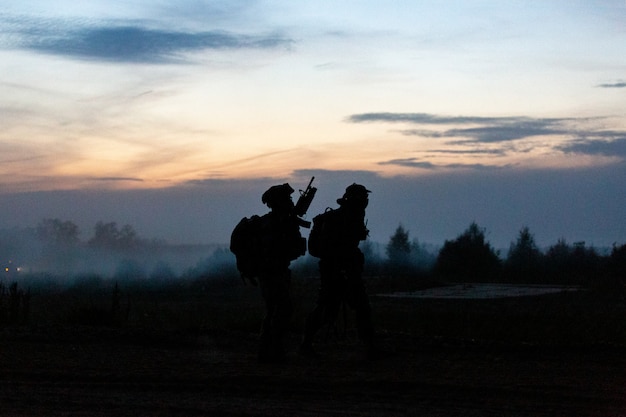 Les soldats de l'action silhouette marchant détiennent des armes l'arrière-plan est la fumée et le coucher du soleil et la balance des blancs