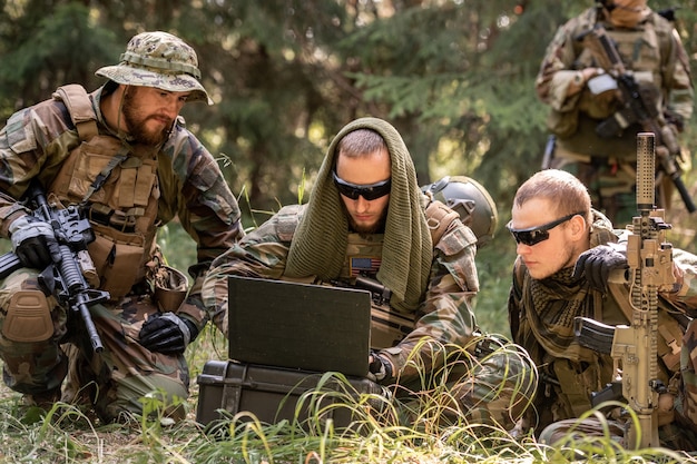 Soldats américains de l'armée en tenue de camouflage assis sur le sol et utilisant un ordinateur portable tout en discutant d'autres actions