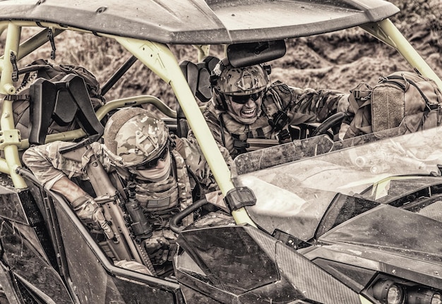 Des soldats d'infanterie modernes armés, des membres d'élite des forces spéciales, des mercenaires de compagnies militaires privées conduisant extrêmement un véhicule de patrouille dans le désert sur un terrain accidenté. Pousse désaturée et recadrée